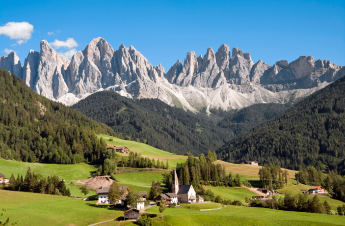 a small village surrounded by green with the Dolomite Mountains behind