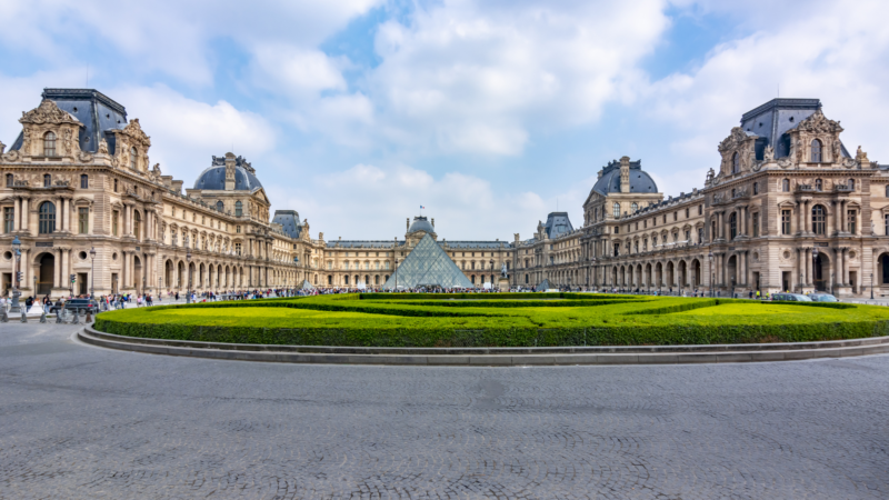 a historic building with a modern pyramid in the courtyard