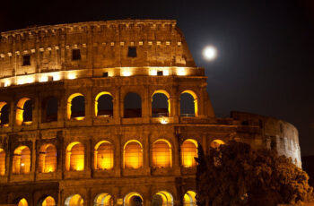 outside the Colosseum lit up at night with the moon behind it