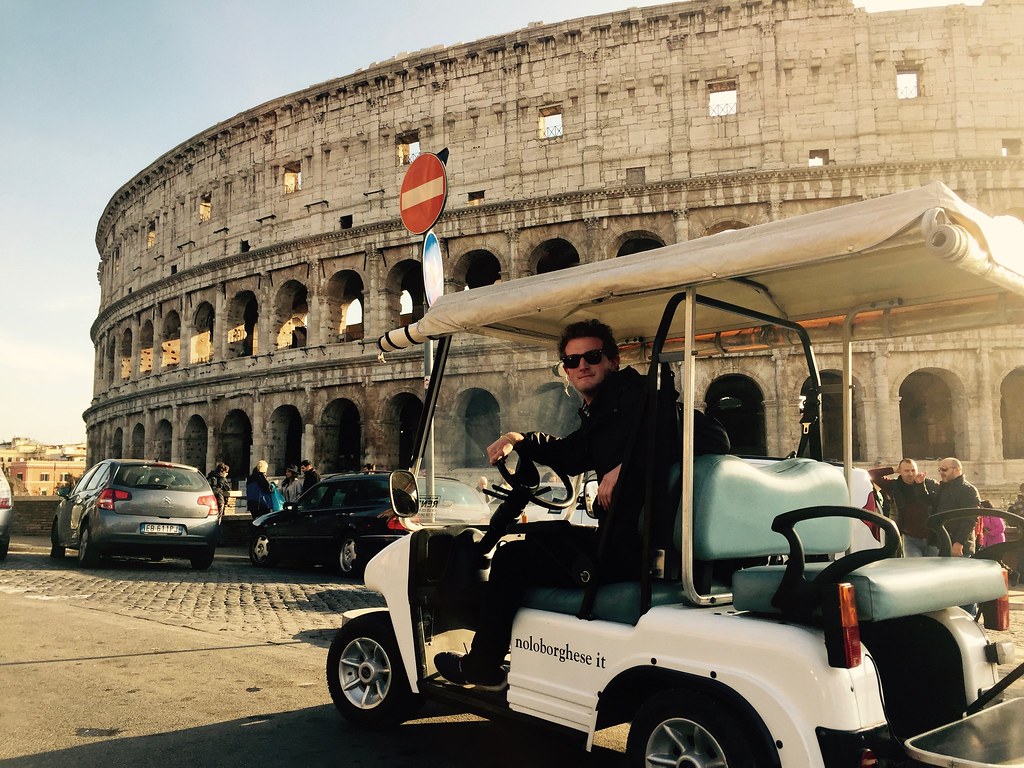 man in golf cart in front of colosseum