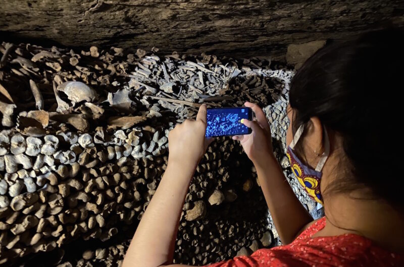 a woman taking a photo of bones in the Paris catacomb