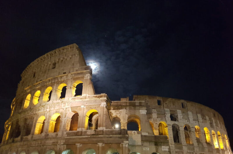 The Colosseum in Rome. The sky is dark and the moon is rising behind it