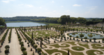 Ornate gardens at the Palace of Versailles with hedges cut in circles and swirls in front of a pool of water