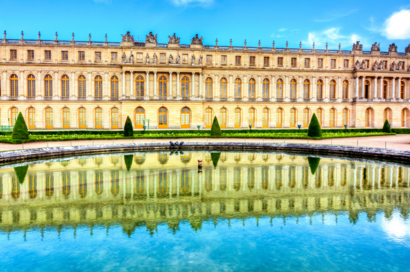 An exterior view of the Palace of Versailles with a pool of water in front of it
