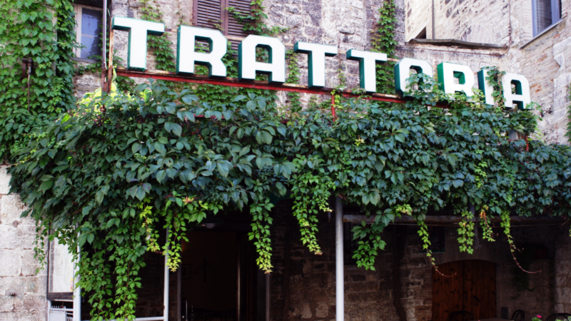 a white 'trattoria' sign about the entrance with ivy hanging below it