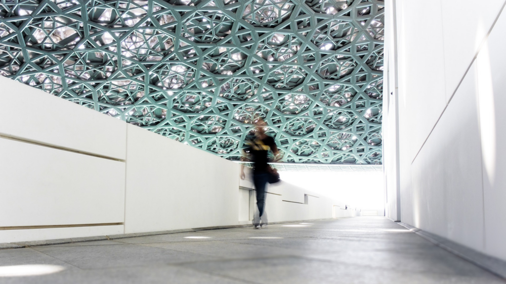 a person walking inside a modern, white building with a green, geometric ceiling