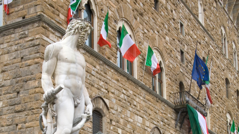 a statue of Neptune and Italian flags hanging from the building behind